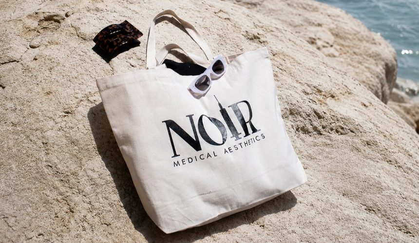 Noir Medical Aesthetics branded tote bag on a sunlit rock by the water